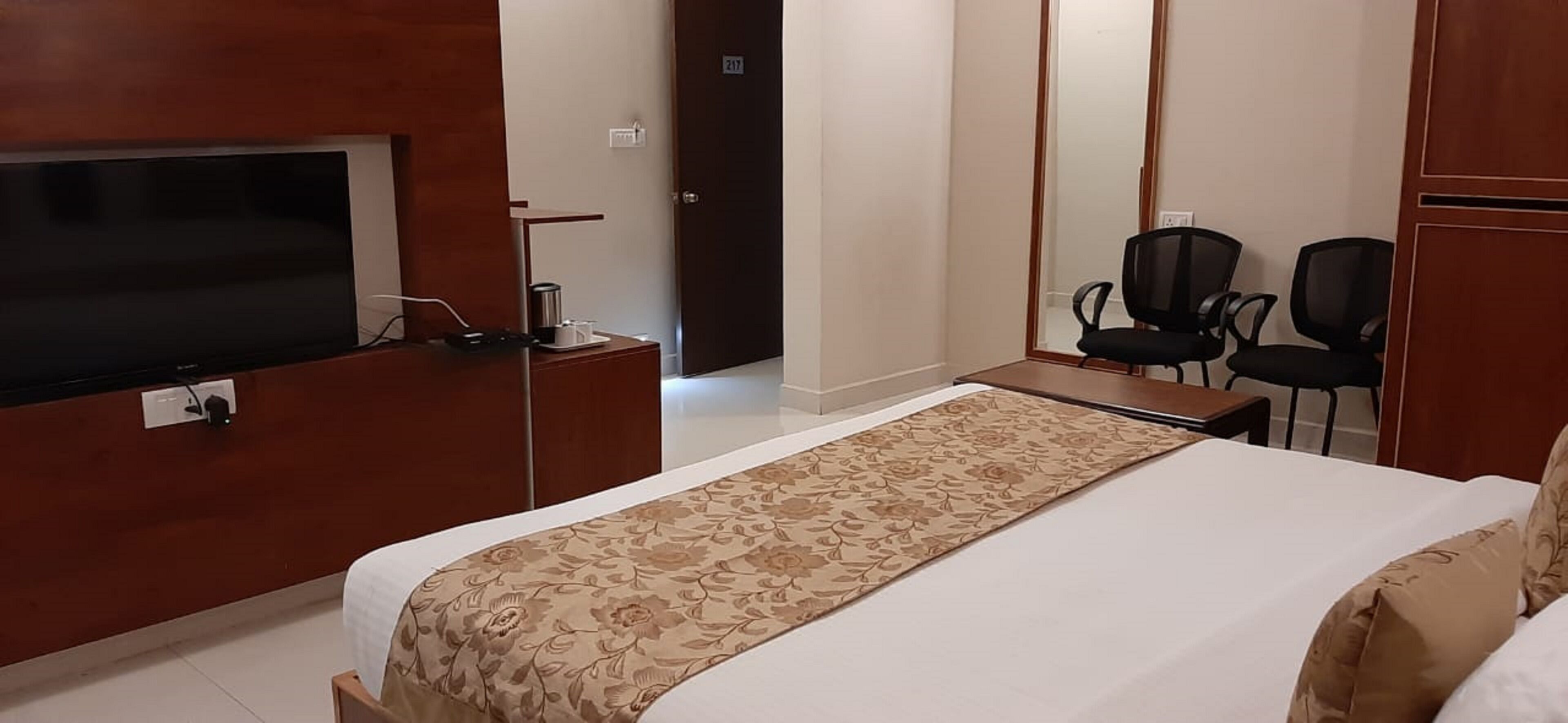 Une chambre d’hôtel avec un grand lit, un téléviseur fixé au mur, un bureau avec une chaise et deux chaises supplémentaires placées contre le mur.