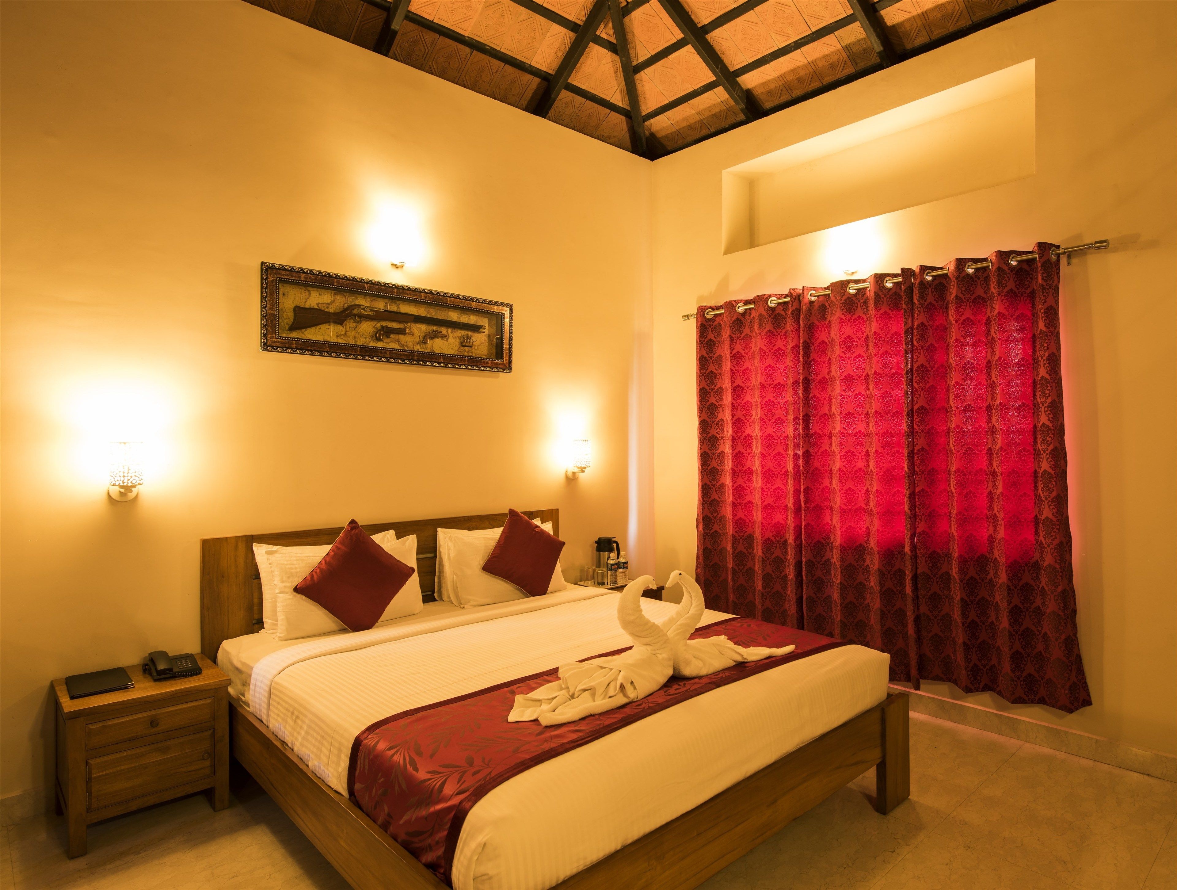 Une chambre d’hôtel avec un lit en bois, une table de chevet, un tableau encadré au mur et un rideau rouge.