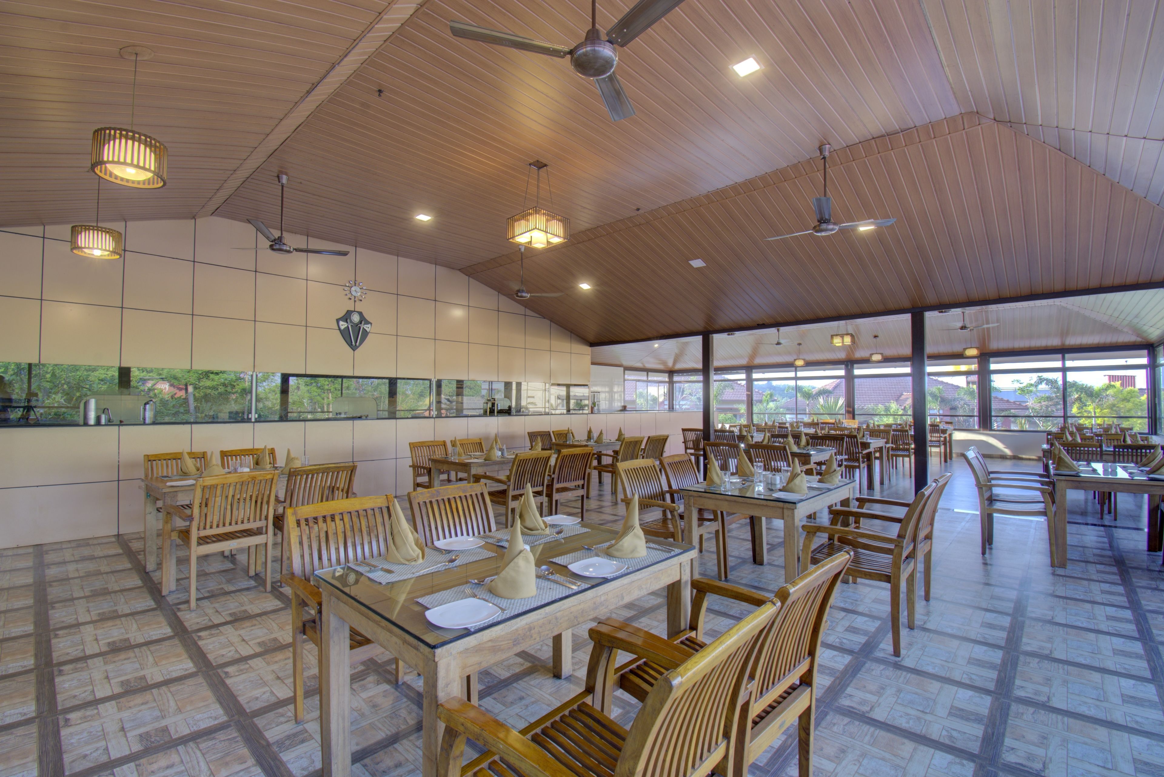 A spacious restaurant with wooden tables and chairs, large windows, and ceiling fans.