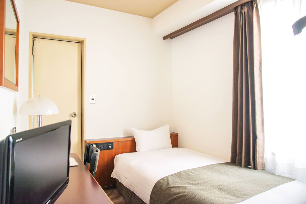 Une chambre d’hôtel avec un lit, un bureau avec un ordinateur, une lampe et une porte.