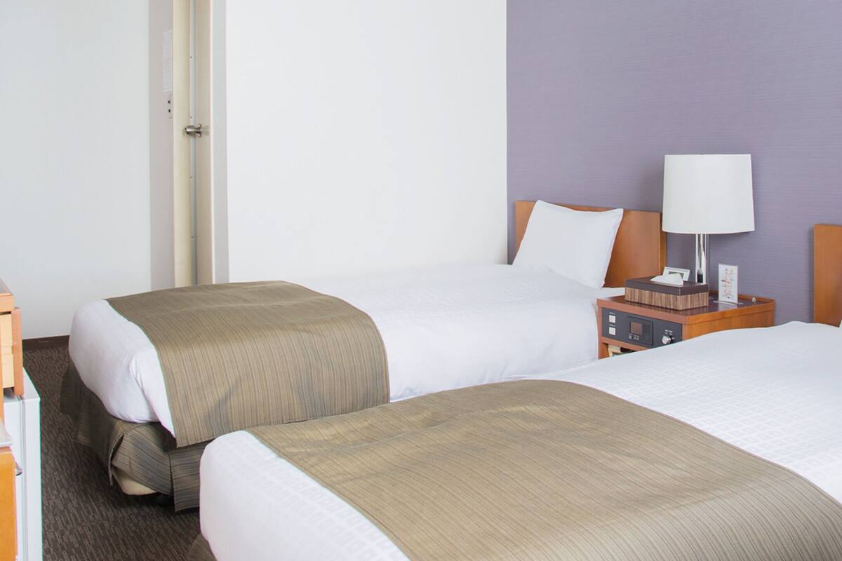 Une chambre d’hôtel avec deux lits, une table de chevet avec une lampe et une commode en bois.