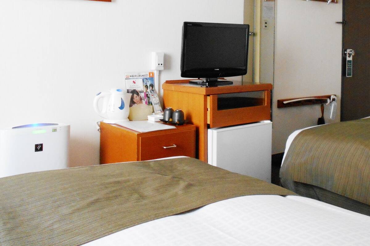 Une chambre d’hôtel avec deux lits, un téléviseur posé sur un meuble en bois, un petit réfrigérateur et un bureau équipé d’une machine à café et d’autres accessoires.