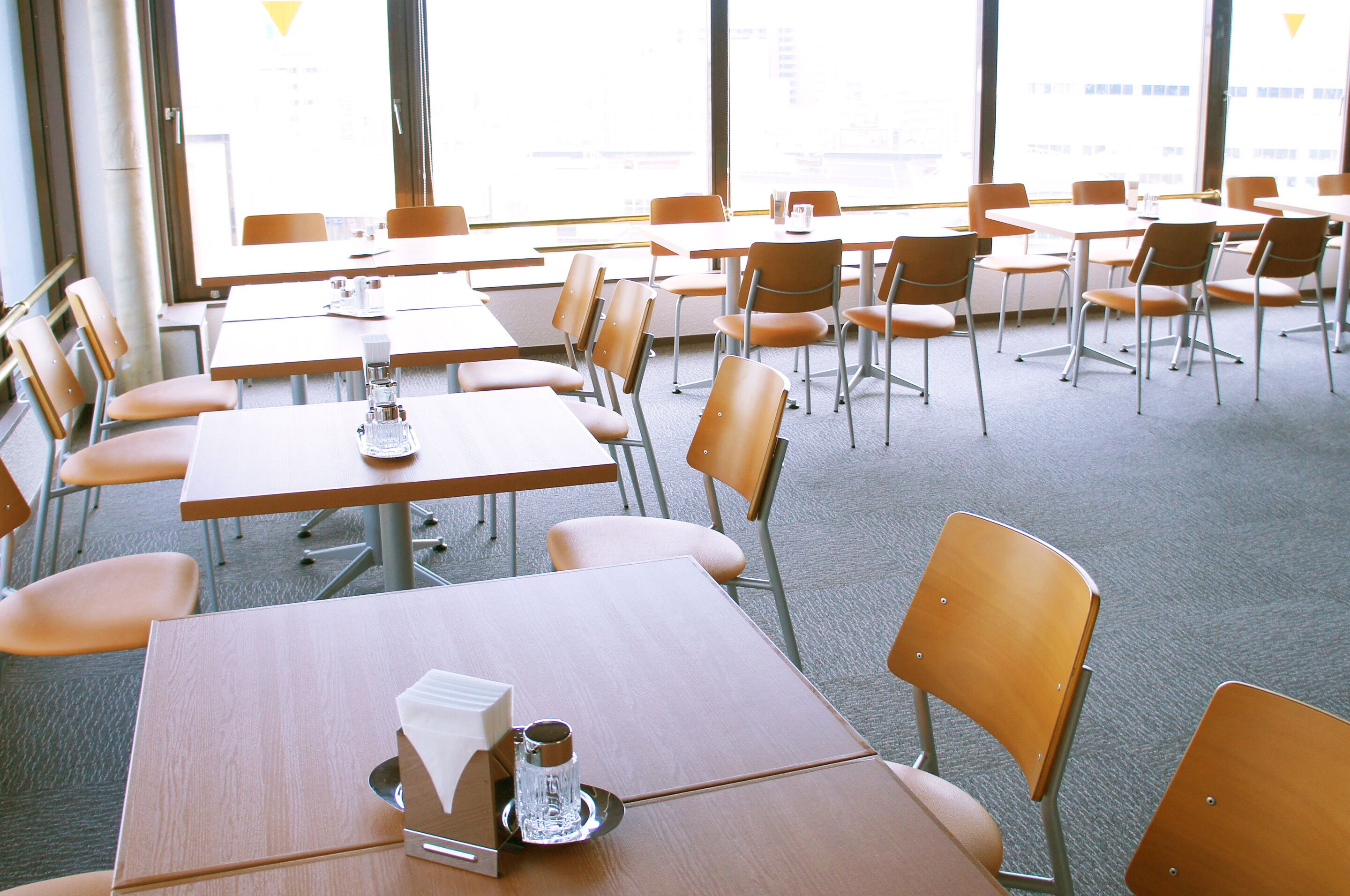 A classroom with tables and chairs arranged in rows, large windows, and a carpeted floor.