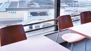 A view from a window with a table and two chairs, overlooking a cityscape with modern buildings and a distinctive curved structure. - Hotel Abest Nagano Ekimae (Nagano)