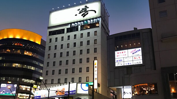 A hotel building with multiple floors, illuminated windows, and various signs including a prominent 'HOTEL BEST' sign. - Hotel Abest Nagano Ekimae (Nagano)