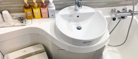Un baño con lavamanos blanco, ducha de mano y encimera de mármol con artículos de aseo.
