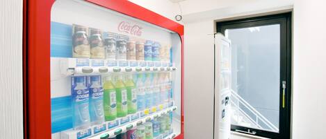 A Coca-Cola vending machine with various beverages and a window to the outside.