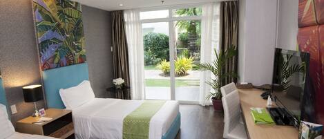 Habitación de hotel con dos camas, un escritorio, una silla, un televisor y vista al jardín.