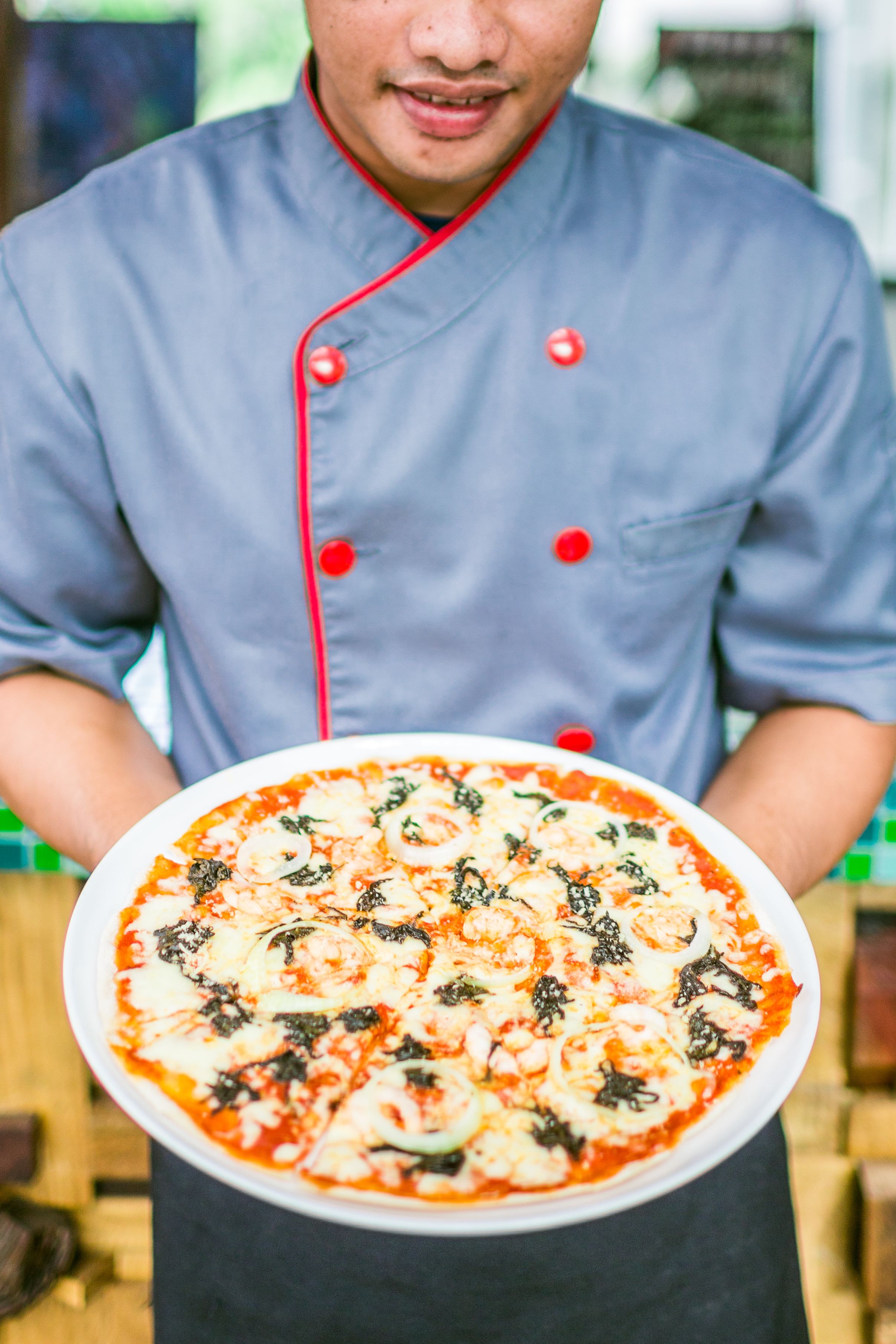 A chef holding a large pizza with toppings.