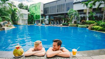 A swimming pool with two people relaxing, a drink, and a coconut on the edge.