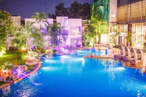 A nighttime swimming pool area with multiple pools, palm trees, and modern buildings. - Aziza Paradise Hotel (Puerto Princesa)