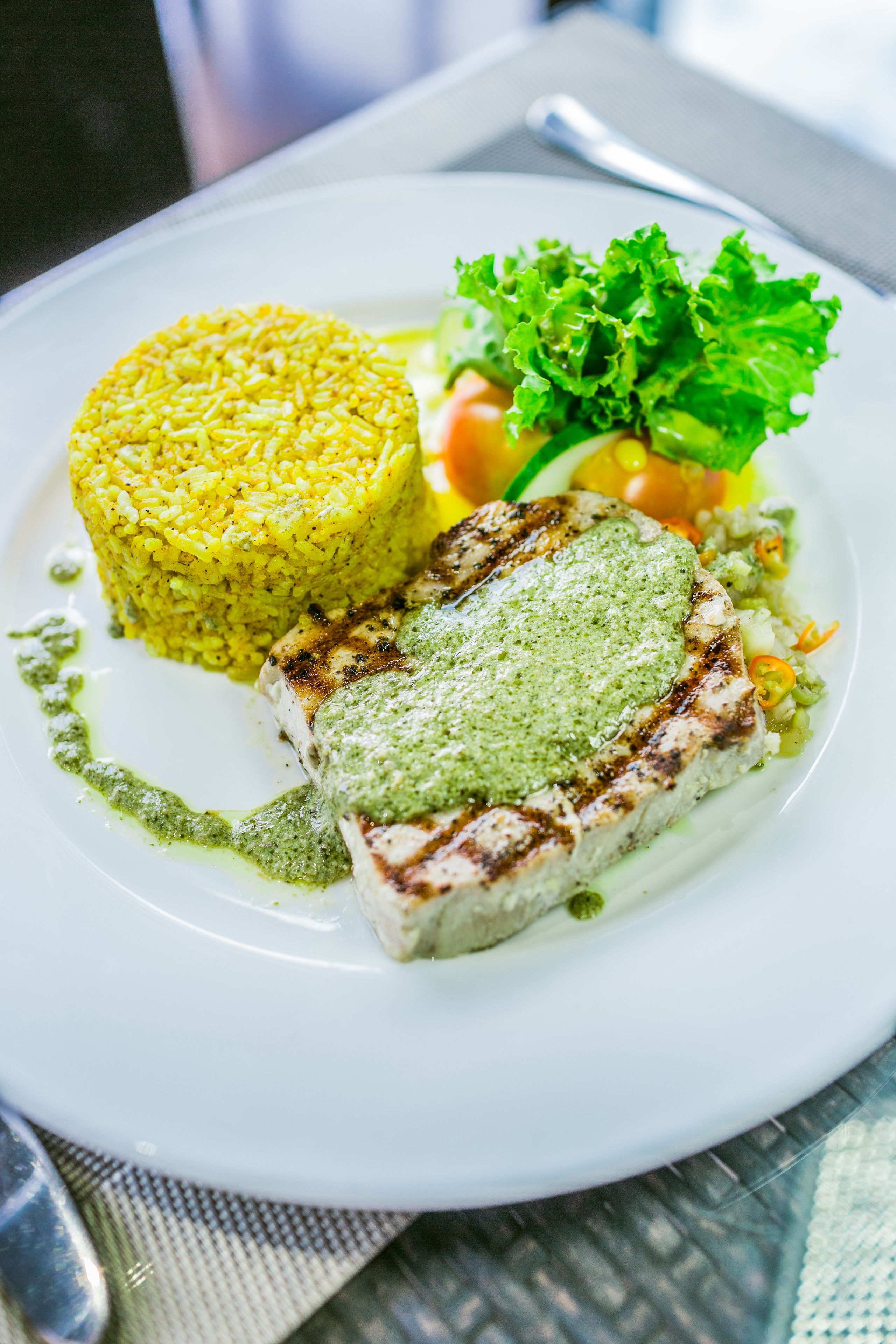 Une assiette contenant du poisson grillé, du riz jaune et une sauce verte.