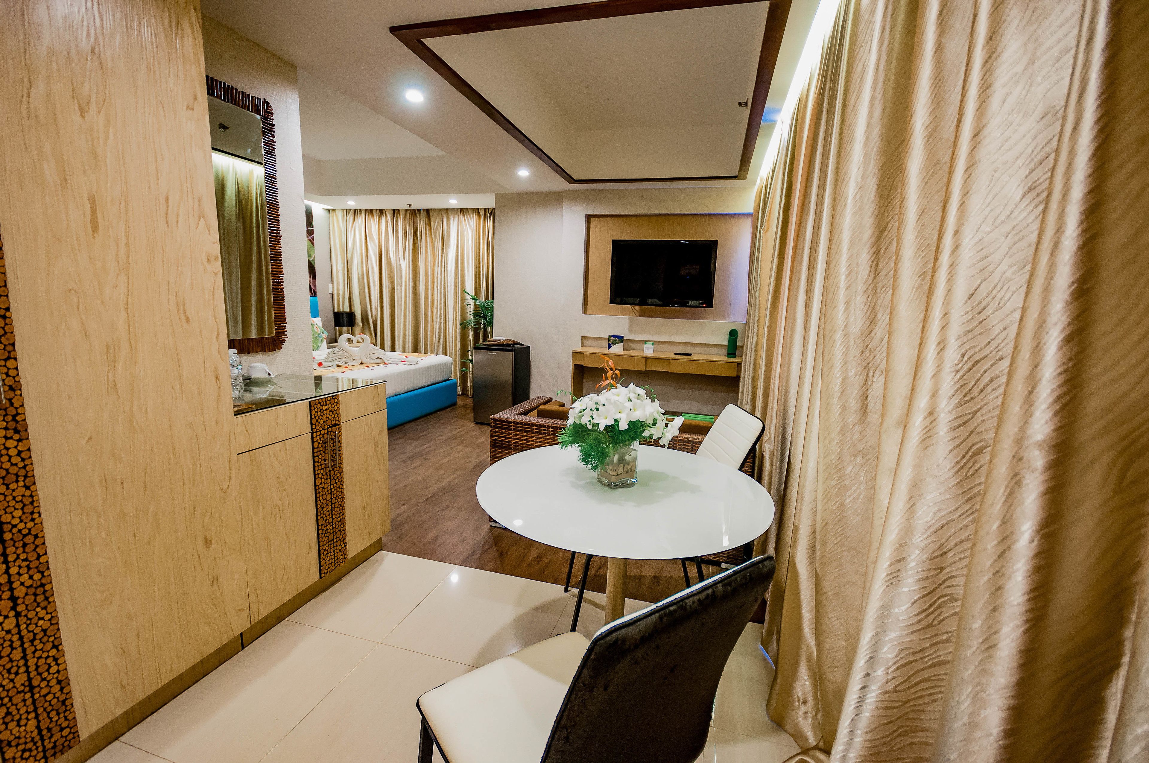 A hotel room with a dining area featuring a round table, chairs, and a vase with flowers.
