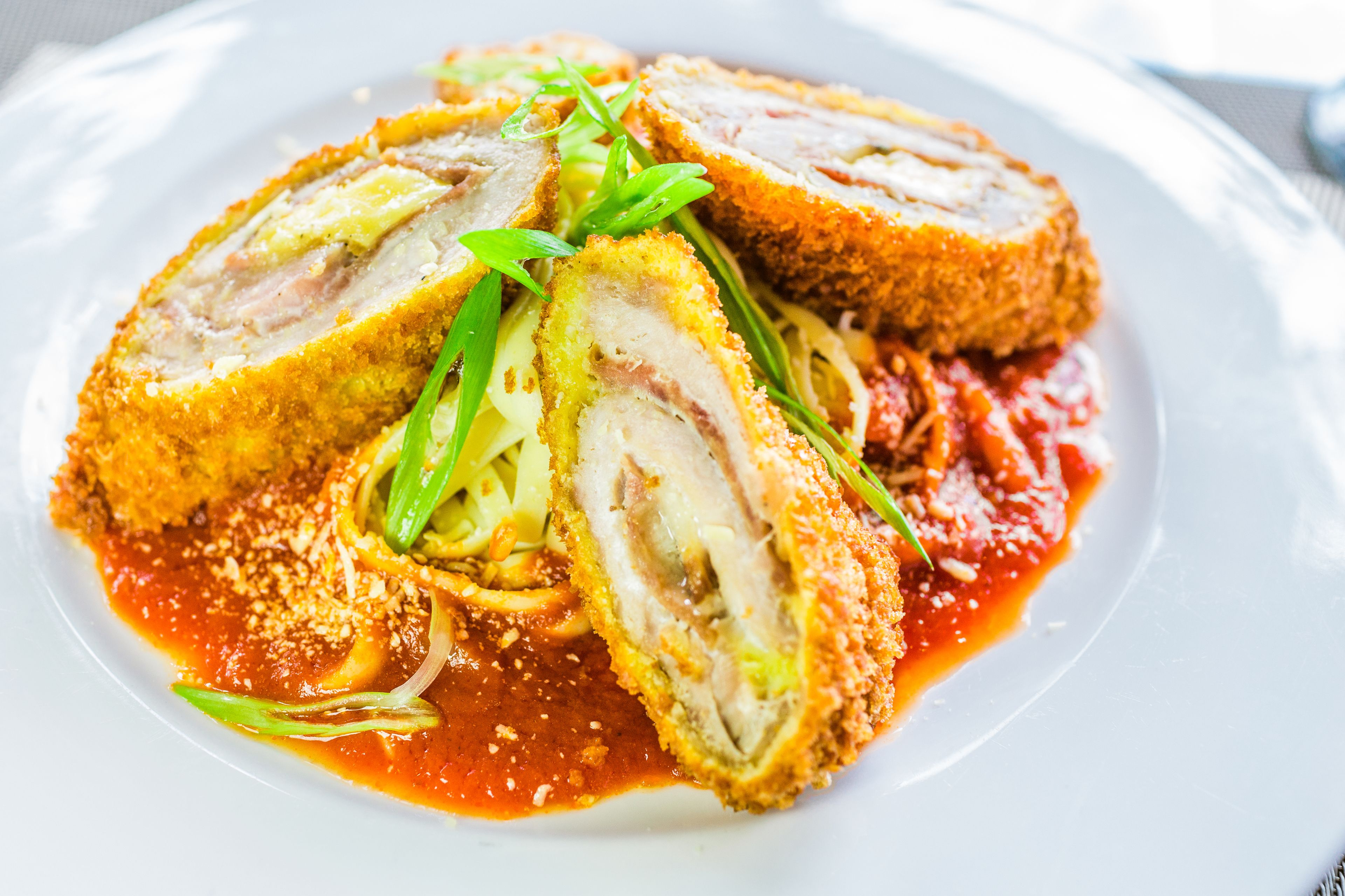 A plate of stuffed chicken rolls with a red sauce and green garnish.