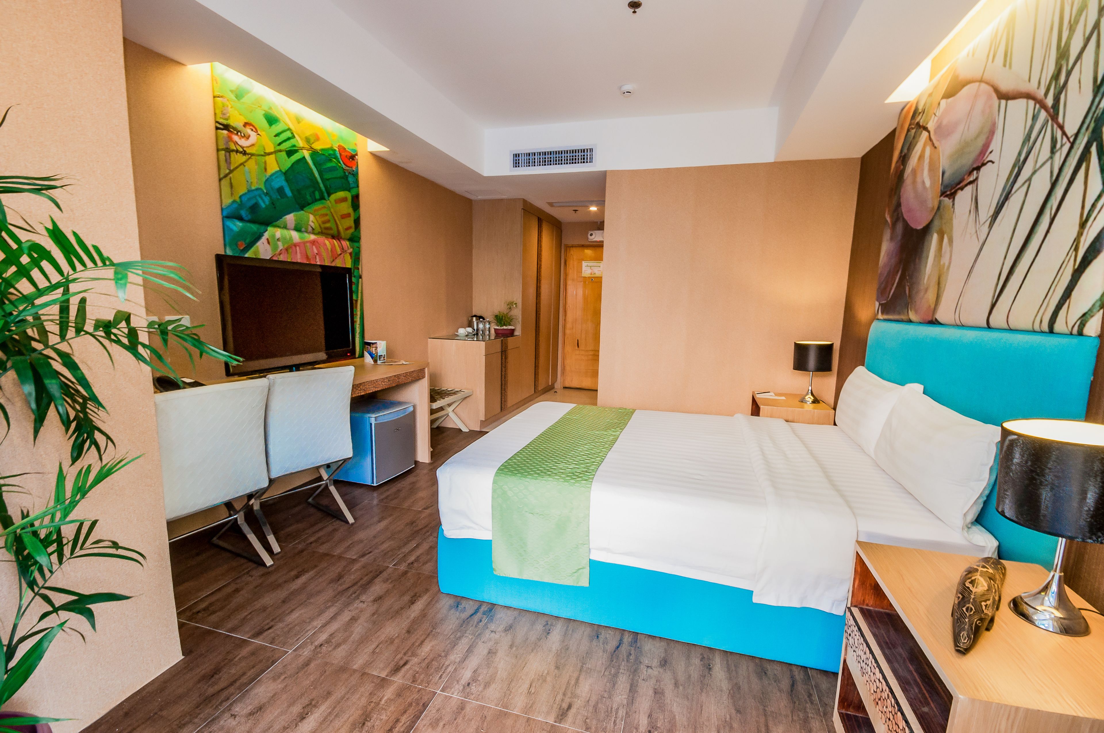 Una habitación de hotel moderna con cama, escritorio, televisor y un amplio ventanal.