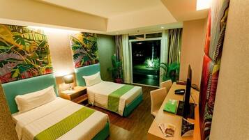 A hotel room with two beds, a desk, a computer, and a view of a garden at night.