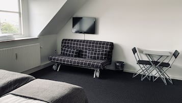 A modern, compact room with a sofa, a small table, and a TV mounted on the wall.