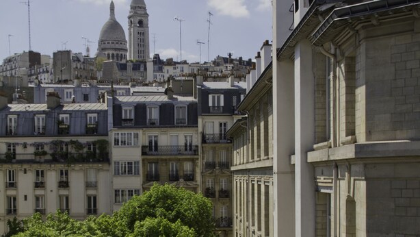 Une vue urbaine avec un dôme et une tour imposants en arrière-plan, entourés d’immeubles à plusieurs étages dotés de balcons.