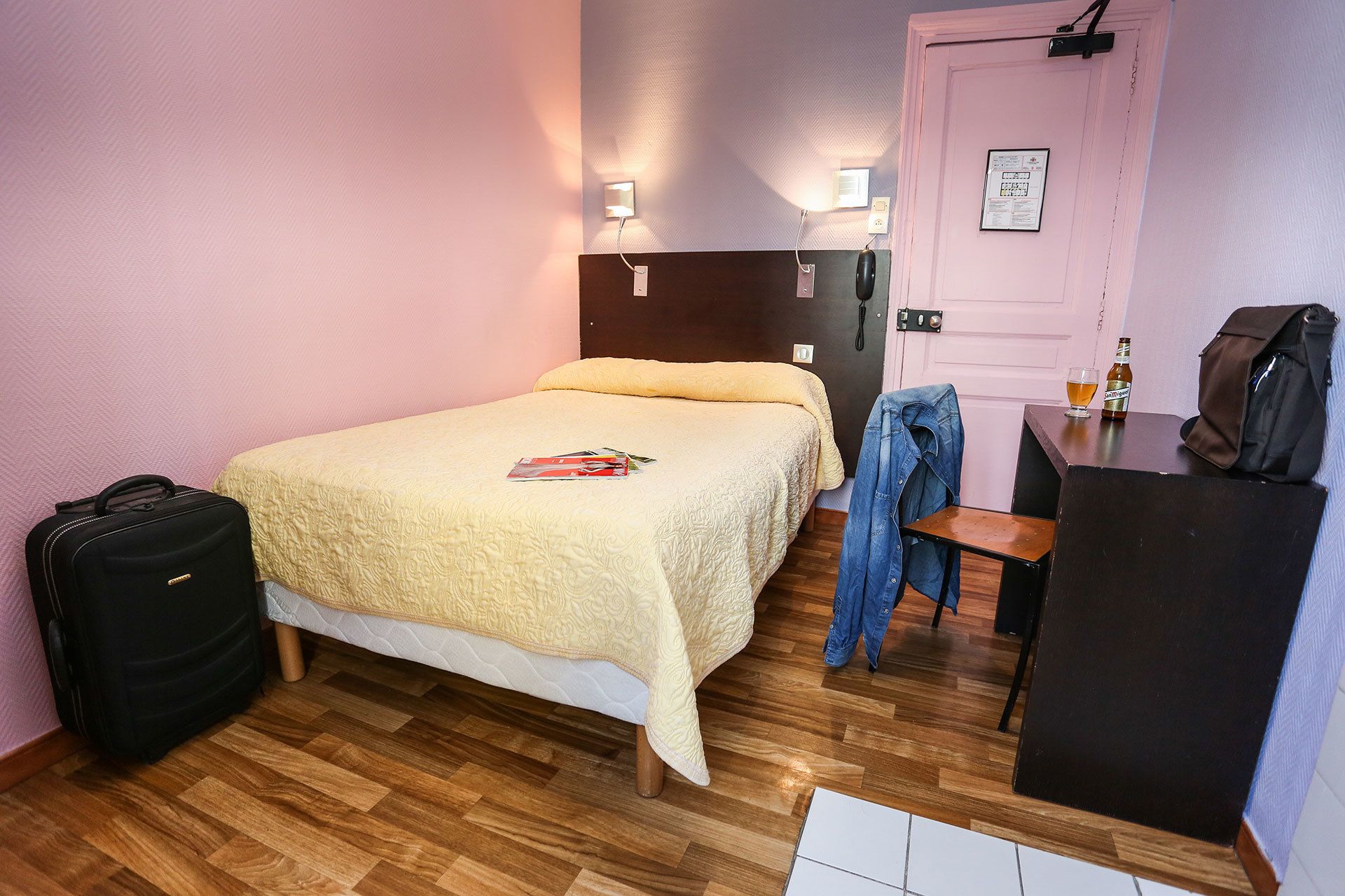 A hotel room with a bed, a desk, a chair, a suitcase, and a door.