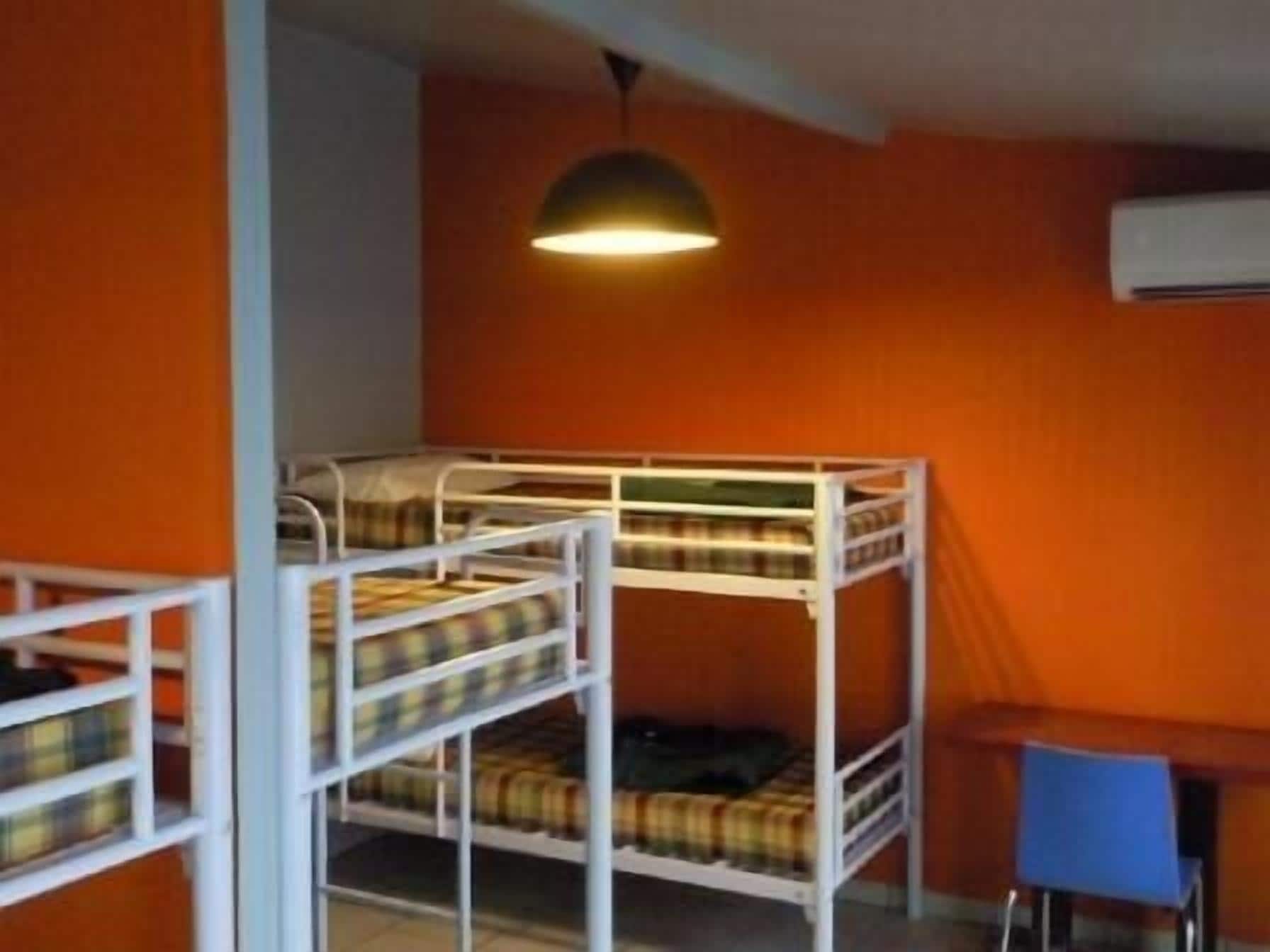 Habitación con literas, una pared naranja, un escritorio y una silla azul.