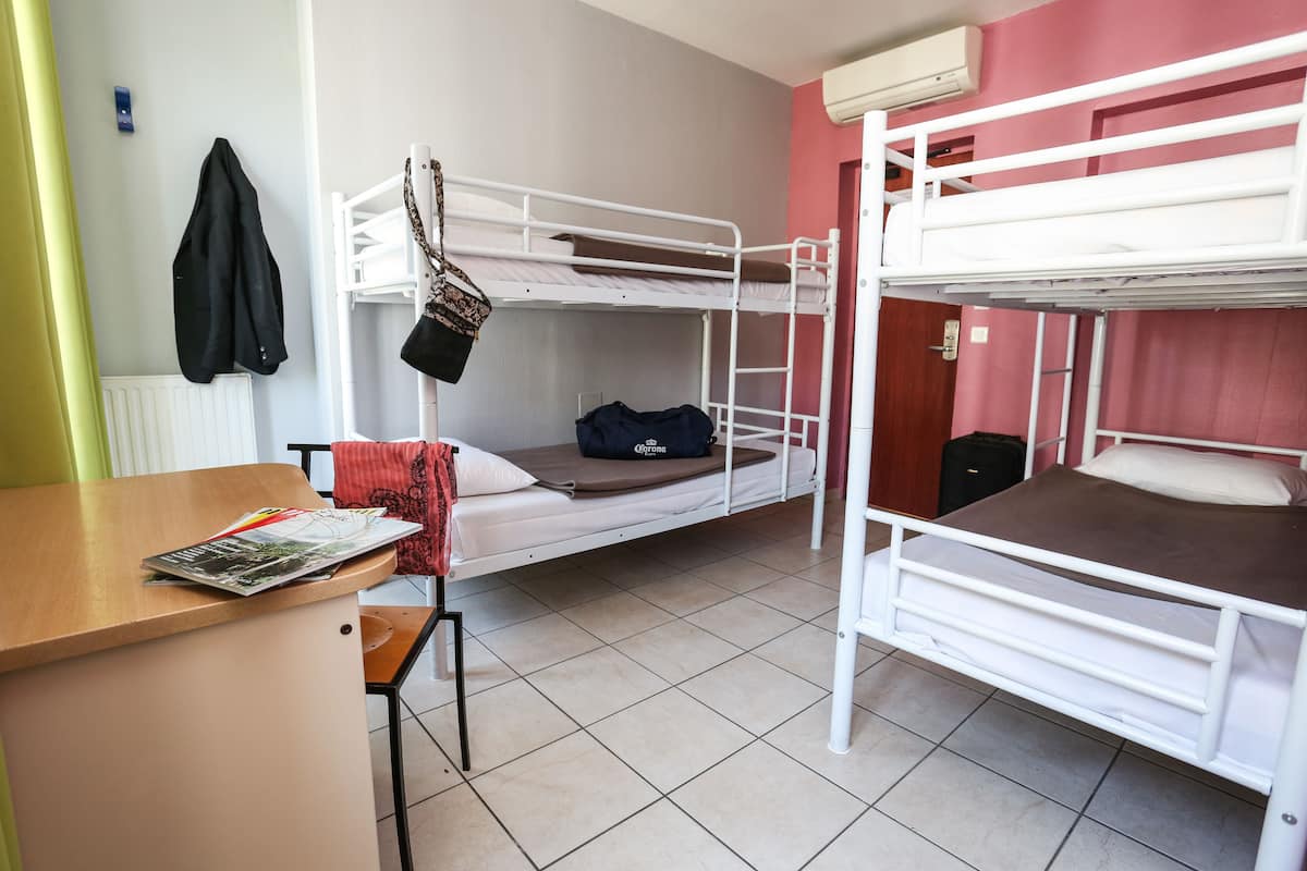 A dormitory room with bunk beds, a wooden desk, and a chair.