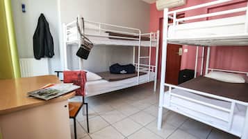 A dormitory room with bunk beds, a wooden desk, and a chair.