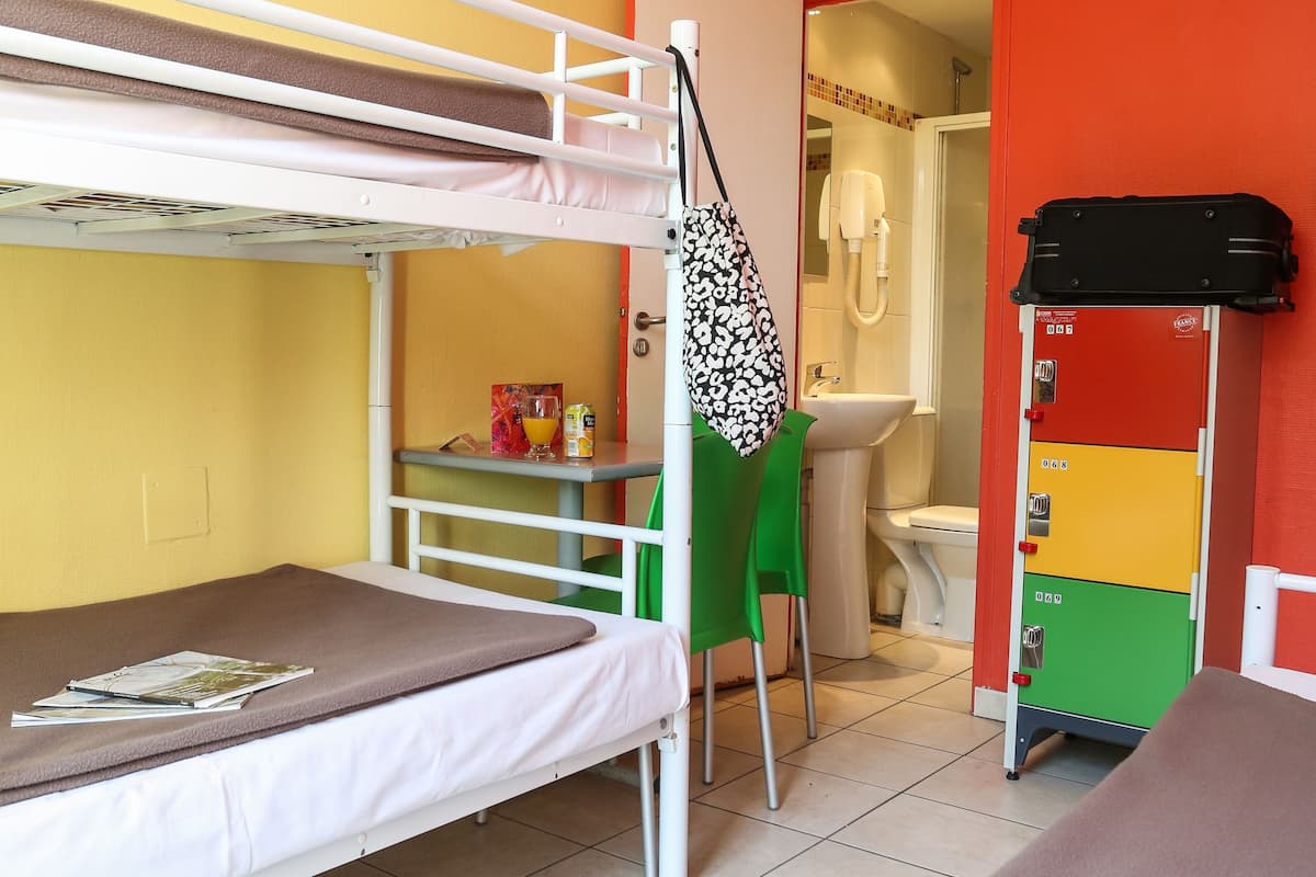 A bunk bed room with a desk and chair, a bathroom with a sink and toilet, and a luggage storage unit.