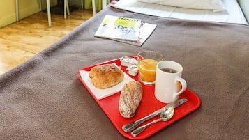 Una habitación con una cama, una bandeja de desayuno con cruasanes, una taza de café y una mesa con sillas.