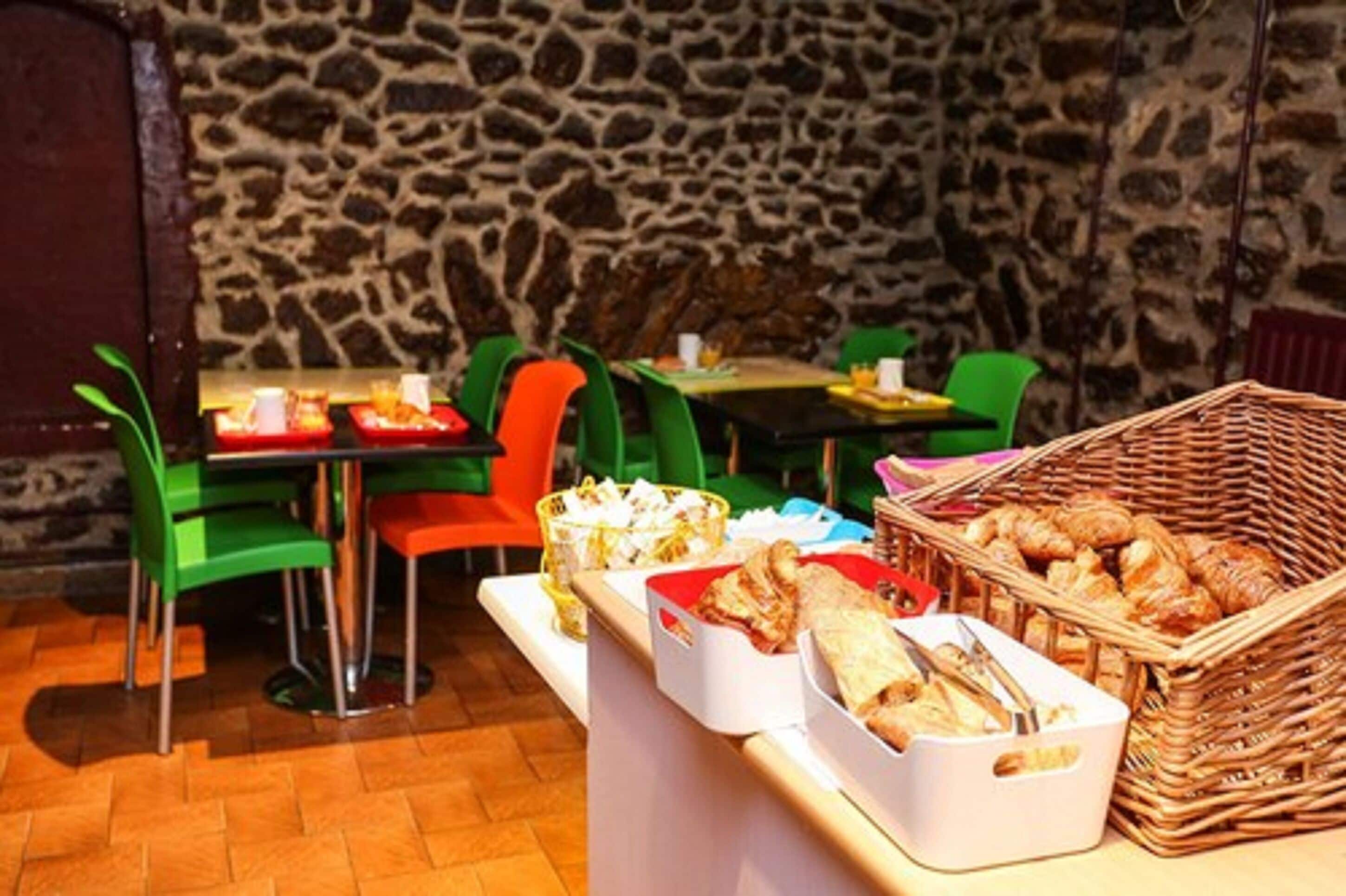 Un restaurante con paredes de piedra, sillas verdes y anaranjadas, y una mesa de buffet con distintos alimentos.