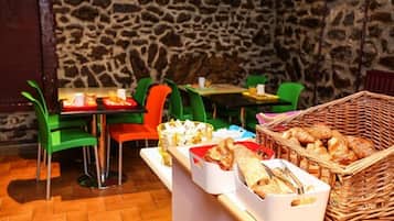 Un restaurante con paredes de piedra, sillas verdes y anaranjadas, y una mesa de buffet con distintos alimentos.