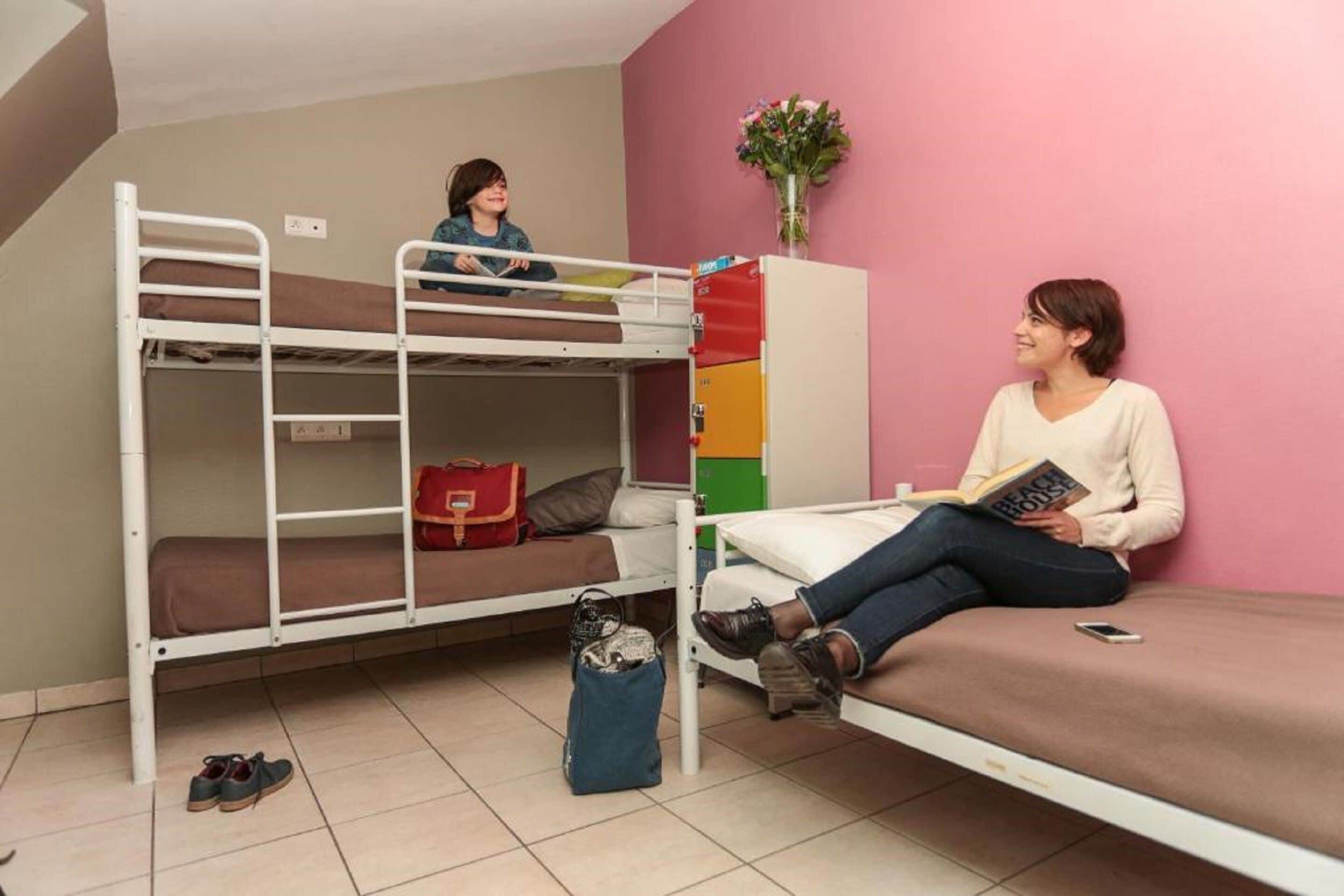 A dormitory room with bunk beds, a desk, and a chair. There are personal items and a bag on the floor.