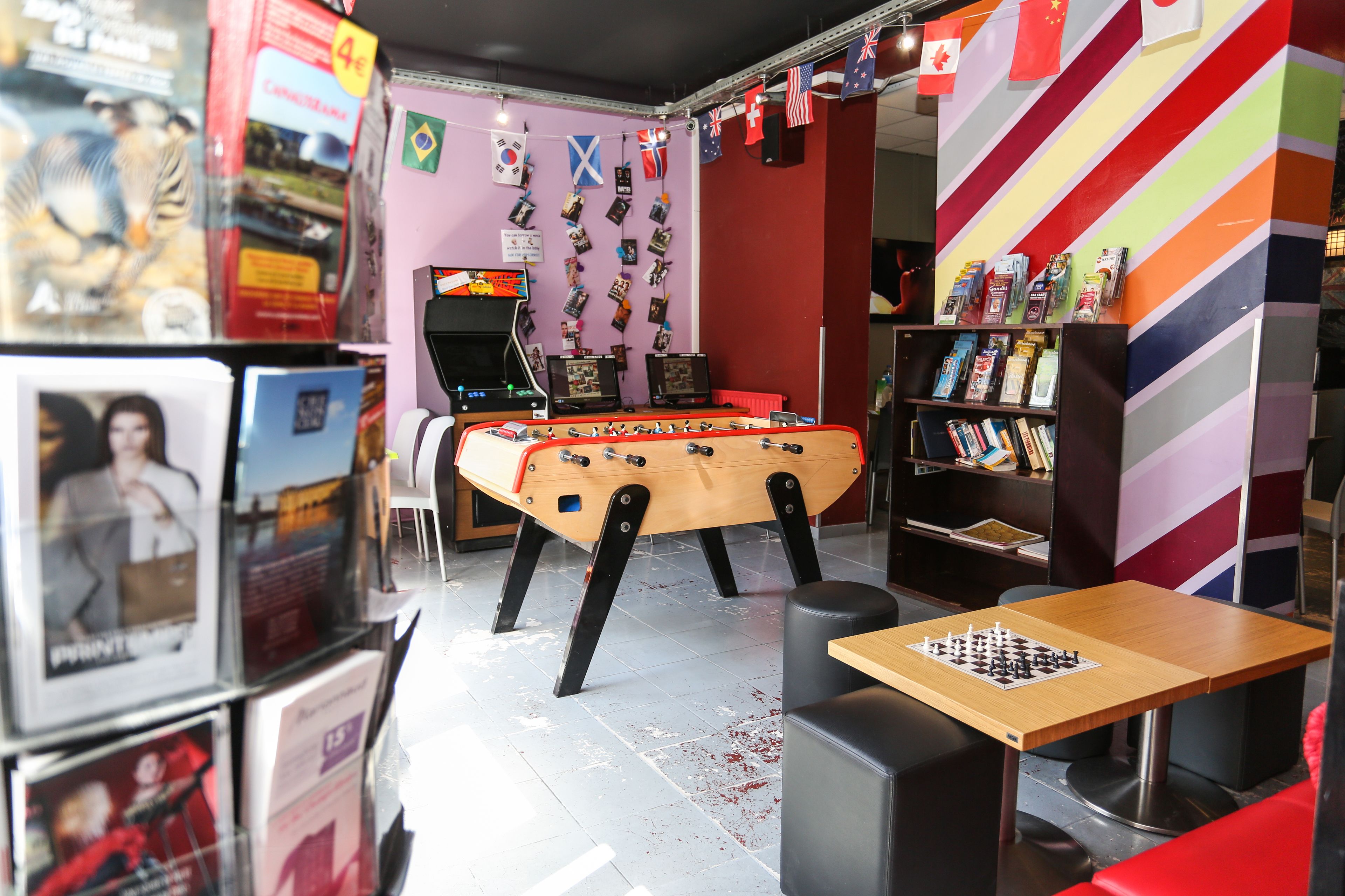 A room with a foosball table, a bookshelf, and a foosball table with a checkered tablecloth.