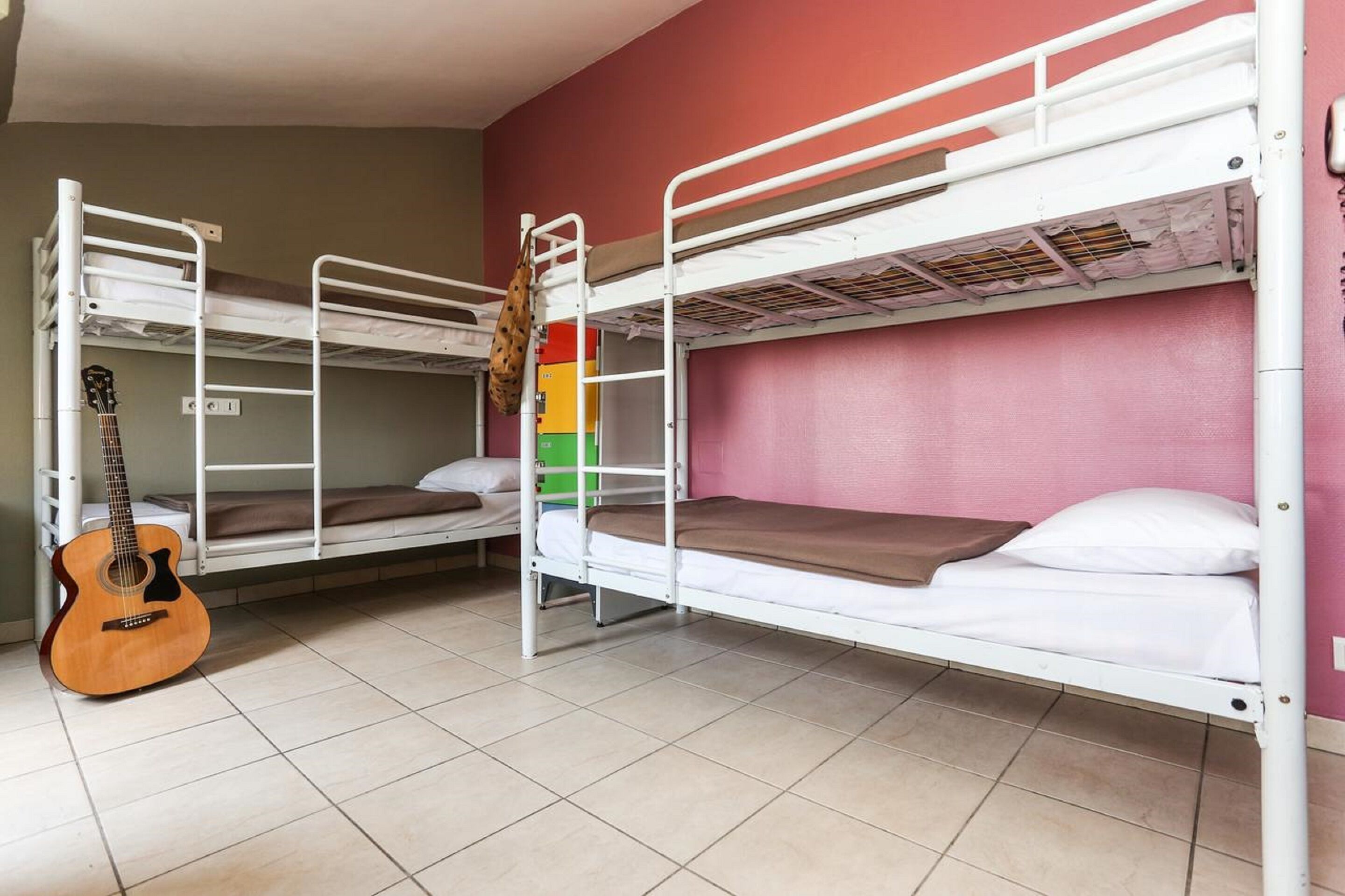 Ein Schlafsaalzimmer mit Etagenbetten, einer Gitarre und einem Wandheizkörper.