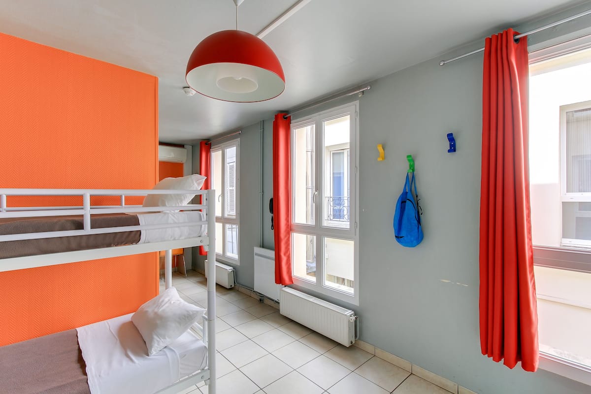 A room with bunk beds, a radiator, a window with red curtains, and a hanging bag.
