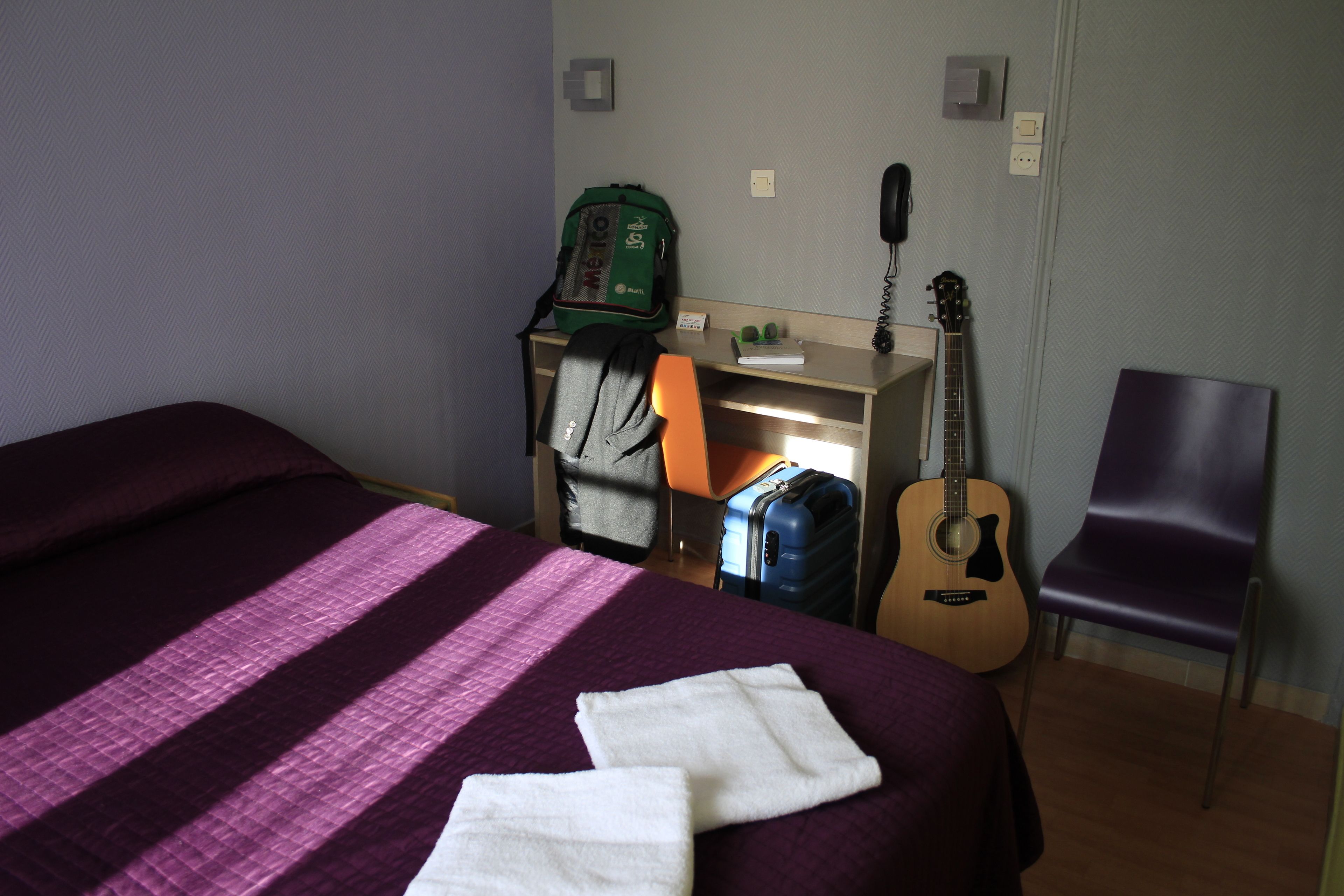 Ein Hotelzimmer mit Bett, Gitarre, Koffer und Stuhl.