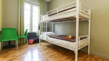 Ein Schlafraum mit Etagenbetten, einem grünen Stuhl, einem Koffer und Frühstücksgebäck auf dem Bett.