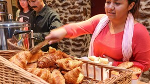 Un panier en osier rempli de viennoiseries et de pain, posé sur une table devant un mur en pierre.