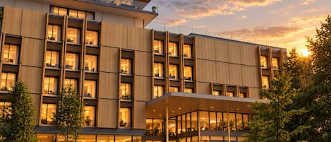A modern hotel with multiple floors, large windows, and a well-lit entrance.