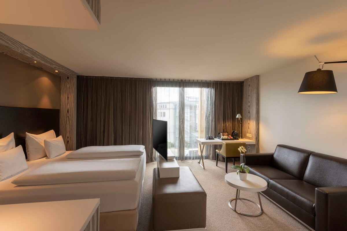 Habitación de hotel con dos camas, un sofá, un escritorio y una televisión.