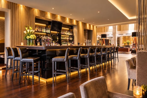 A bar area with a long counter, multiple bar stools, and a variety of bottles. - Grand Hotel Palace Schönbrunn (Vienna)