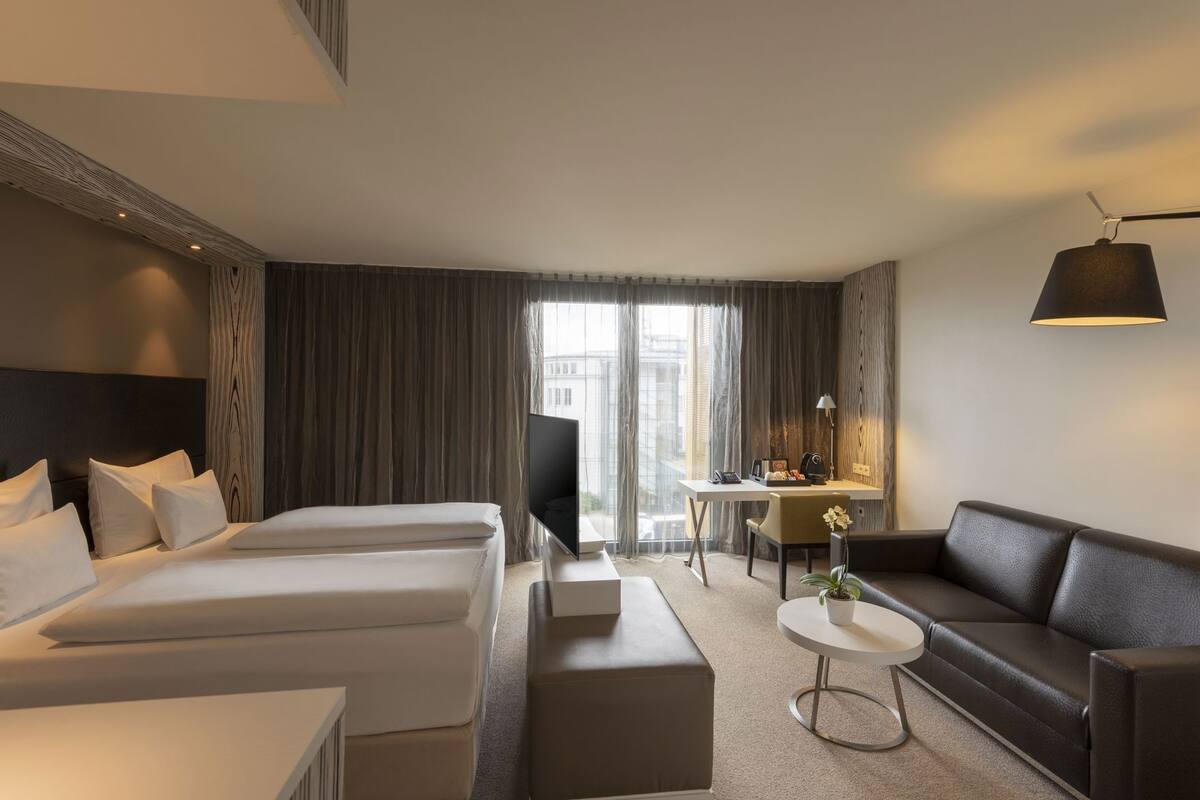A hotel room with two beds, a desk, a sofa, a coffee table, and a TV.
