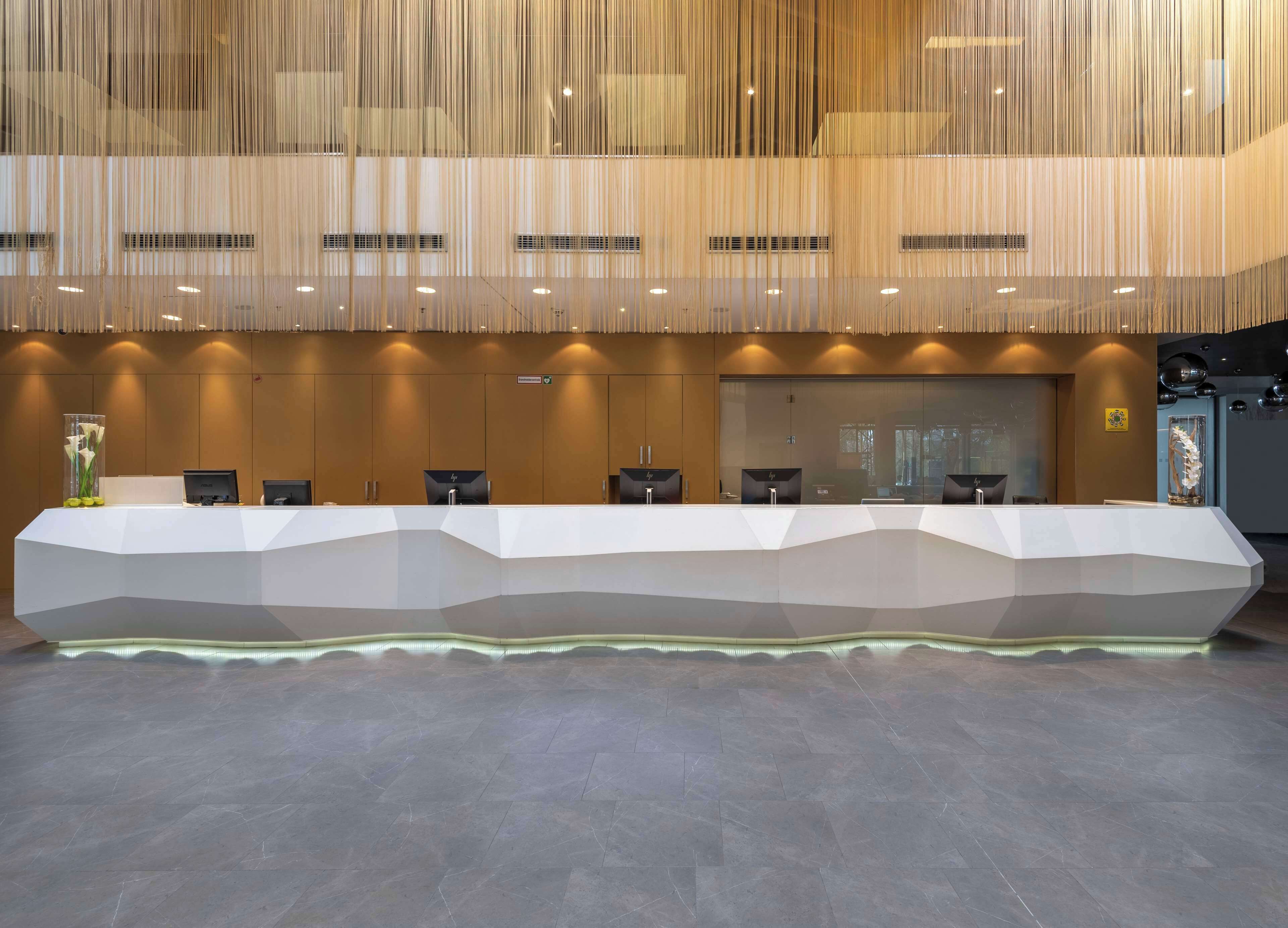 Un mostrador de recepción con diseño moderno, varias estaciones de trabajo con computadoras y un separador de vidrio.
