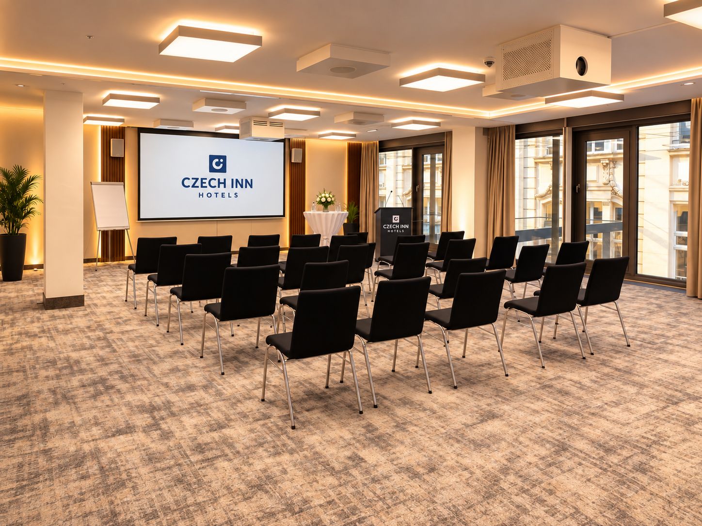 A conference room with a projection screen, black chairs, and a podium labeled 'Czech Inn Hotels'.