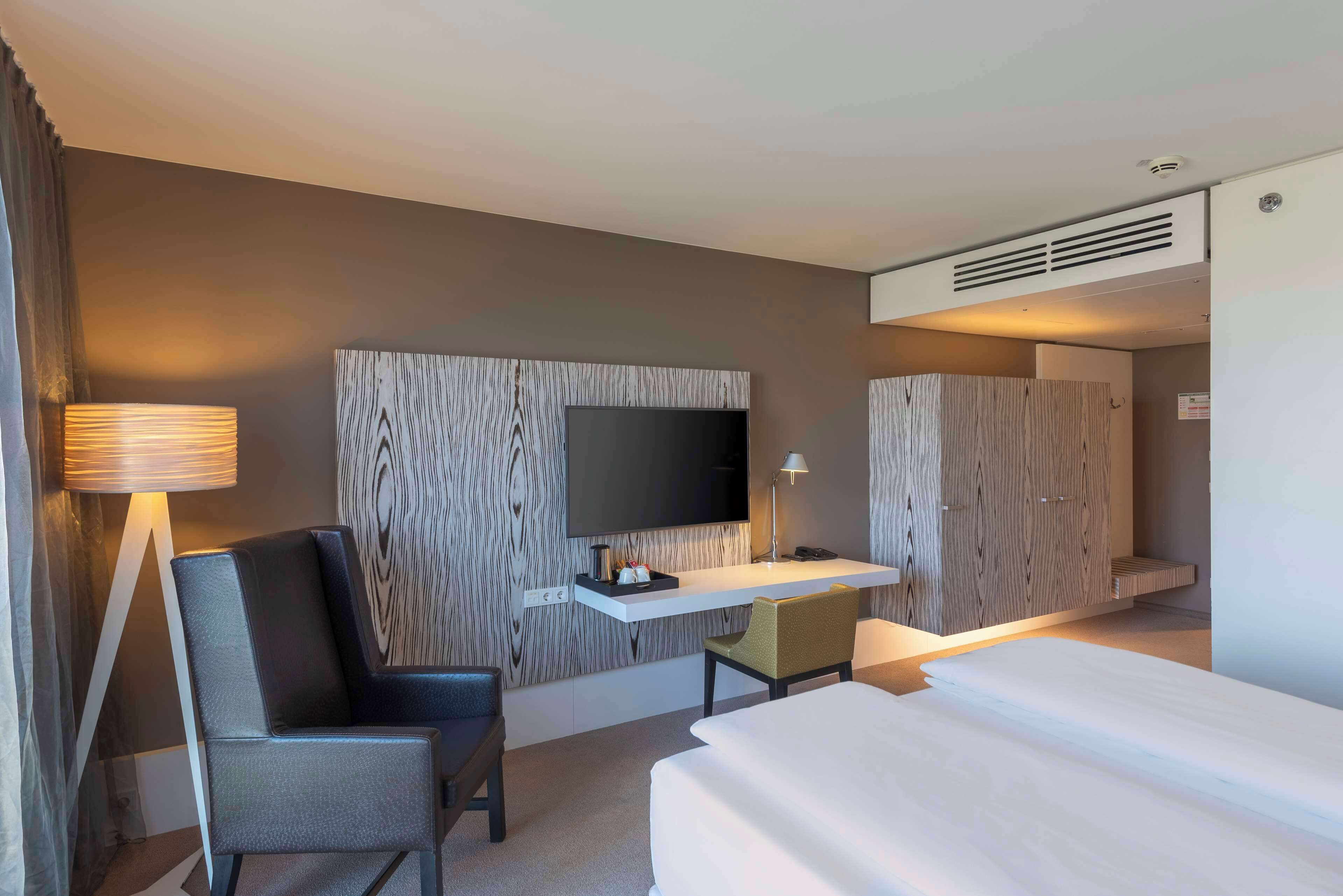 Habitación de hotel con cama, escritorio con televisor de pantalla plana, silla, lámpara y armario.