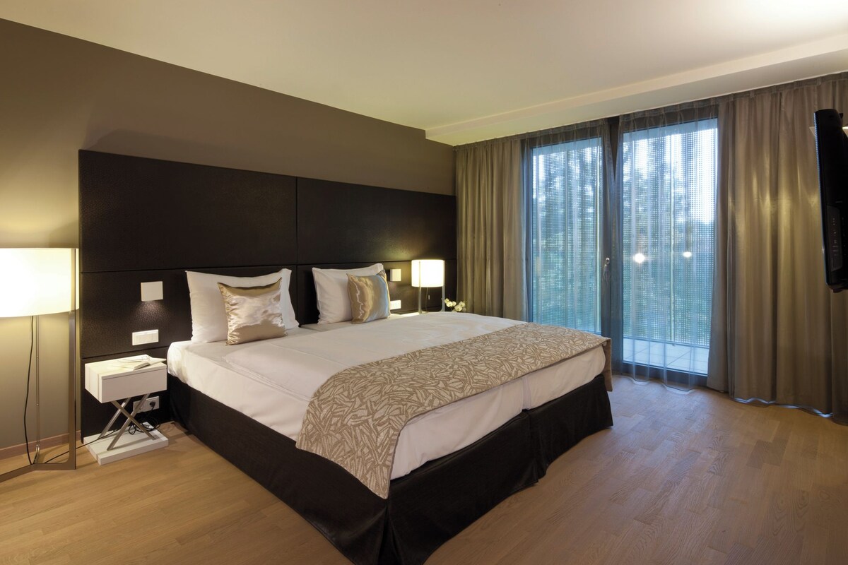 Habitación de hotel con una cama grande, dos lámparas de noche, televisión y vistas a la ciudad por la ventana.