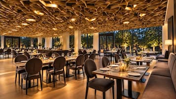 A spacious dining area with high ceilings and modern lighting. Tables are set for dining with chairs.