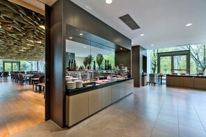 A modern breakfast bar with a glass enclosure, surrounded by seating and large windows. - Doubletree by Hilton Vienna Schonbrunn (Vienna)