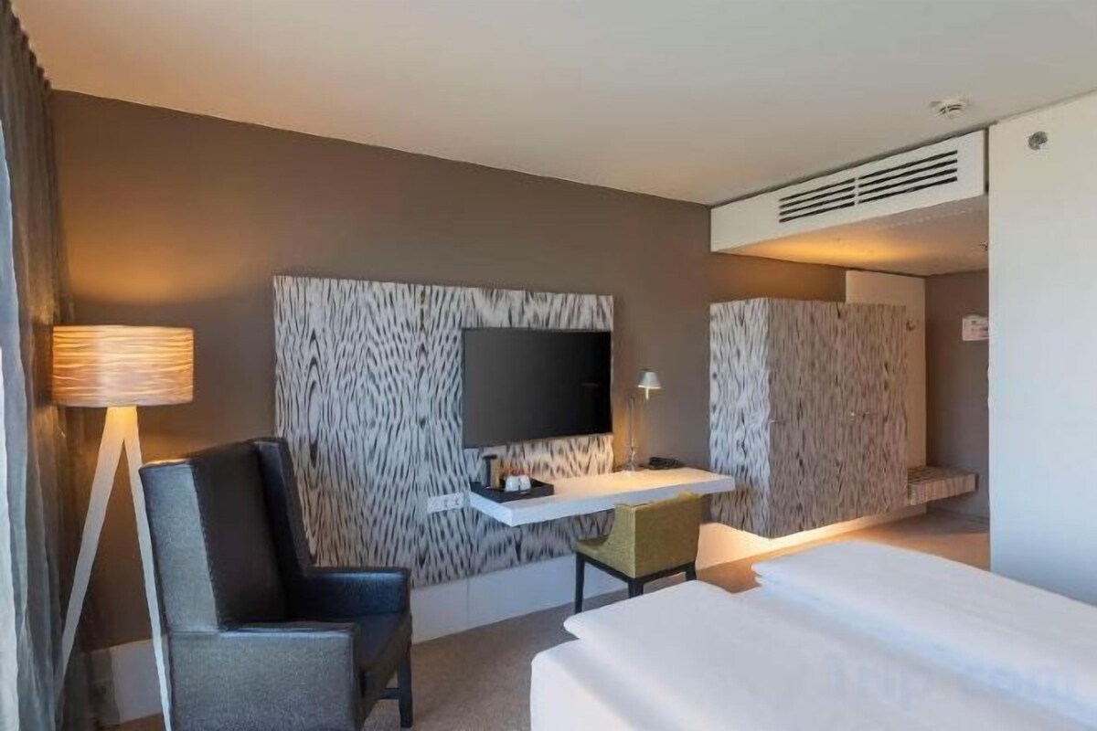 Habitación de hotel con cama, escritorio, silla, televisor y lámpara.