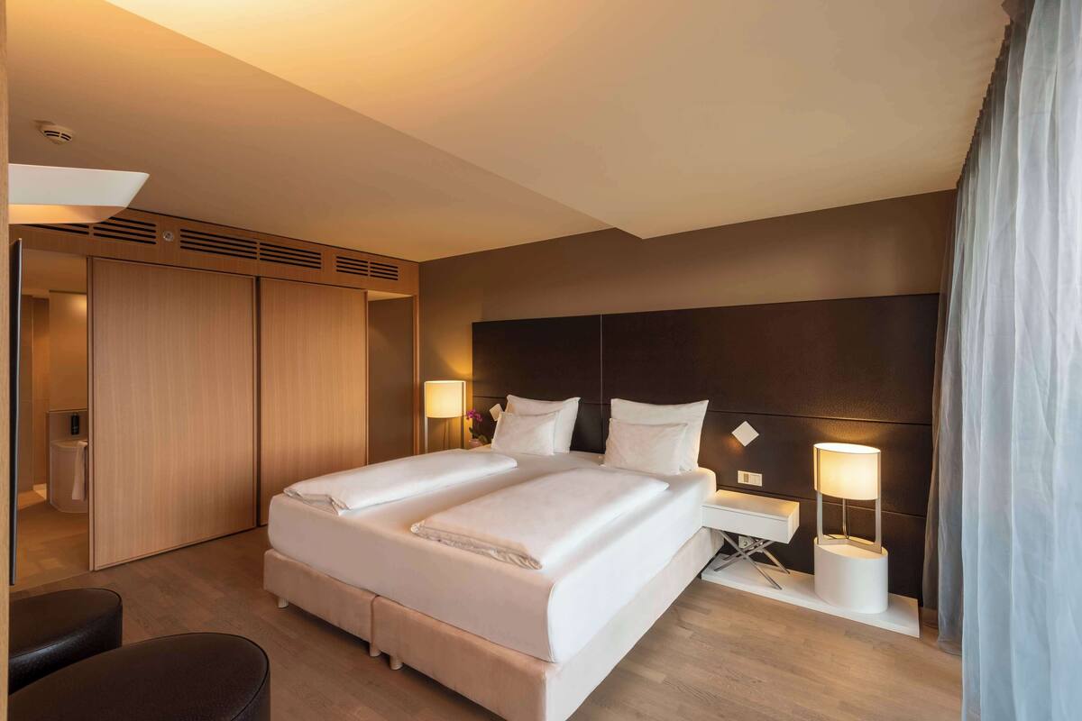 A hotel room with a double bed, bedside tables, a lamp, a wardrobe, and a mirror.
