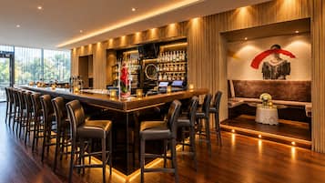 Zona de bar con una barra larga, varios taburetes y una estantería llena de botellas.